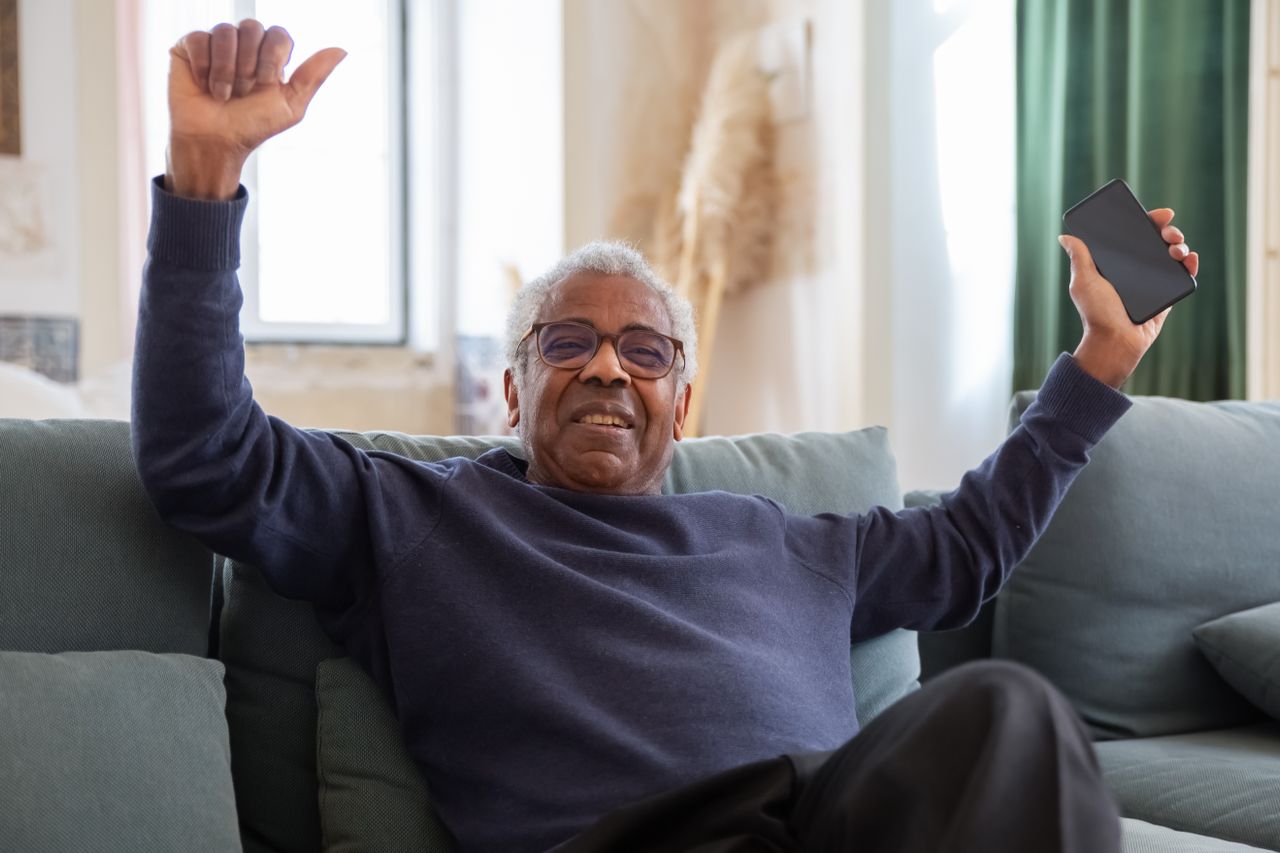 A smiling older man relaxing on a couch with his phone, representing confident retirement planning
